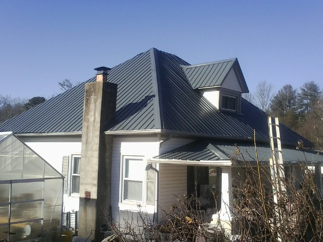 Dark blue standing seam metal roof on a white farmhouse with dormer — Slate & Tile Roof Repair by Roofing Brothers in Pisgah