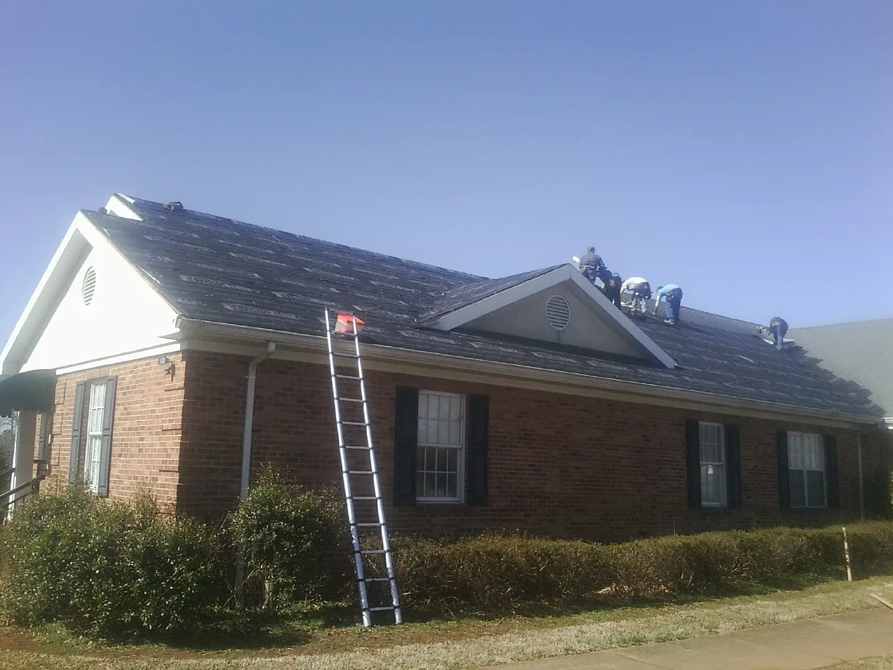 Crew tearing shingles off a brick ranch roof with a ladder set — Emergency Roof Repair work by our crew in Pisgah