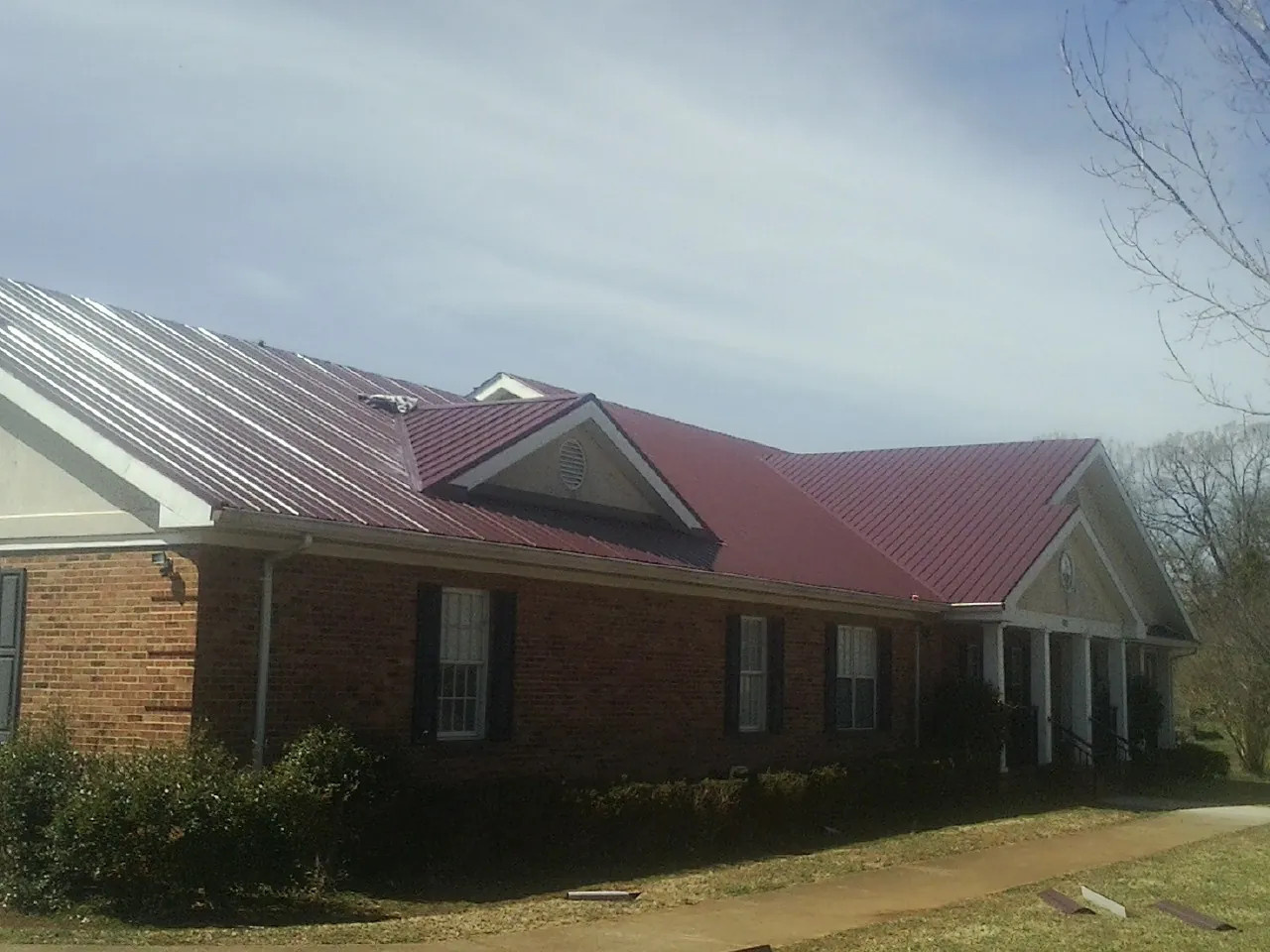 Red metal roof with gabled entries on a long brick building, from a Hail Damage Roof Repair job in Pisgah
