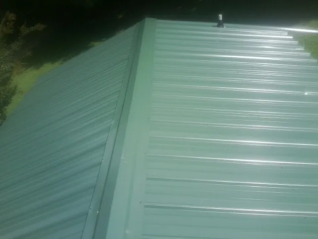 New green metal panels meeting at the ridge of a roof — Flat Roof Repair work by our crew in Pisgah