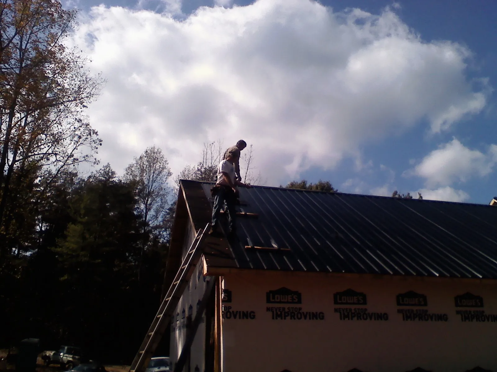 Roofer fastening dark metal panels high against a cloudy sky, from a Roof Inspection job in Pisgah