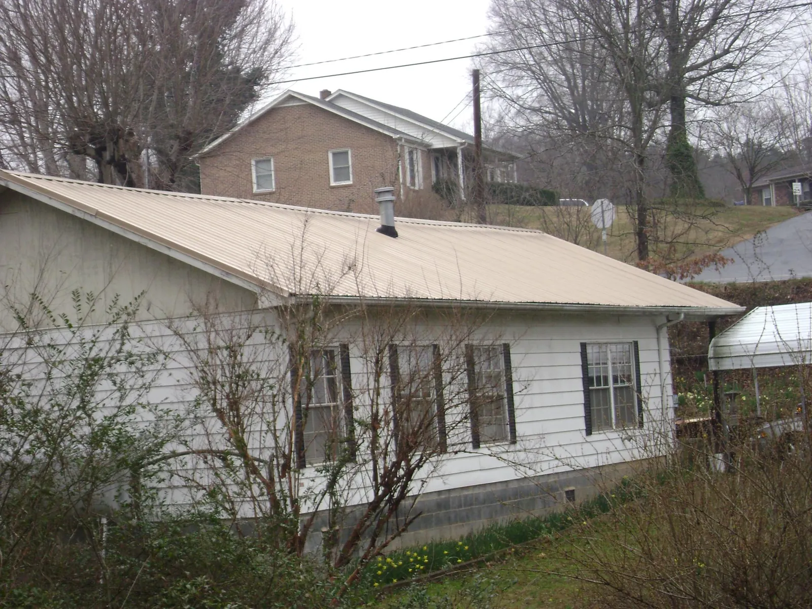 Tan metal roof on a white sided house set into a hillside — Commercial Roofing by Roofing Brothers in Pisgah