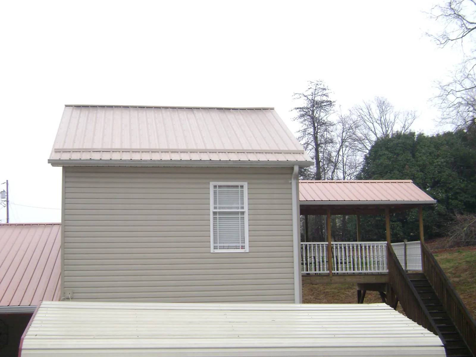 Tan metal roofs on a two story addition and attached porch, from a Roof Replacement job in Pisgah